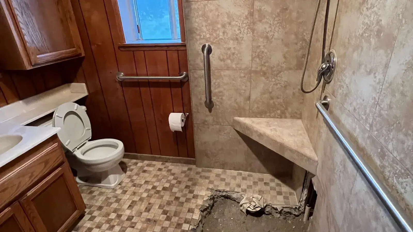 Before: Dated bathroom with wood paneling and a worn tiled shower before remodel