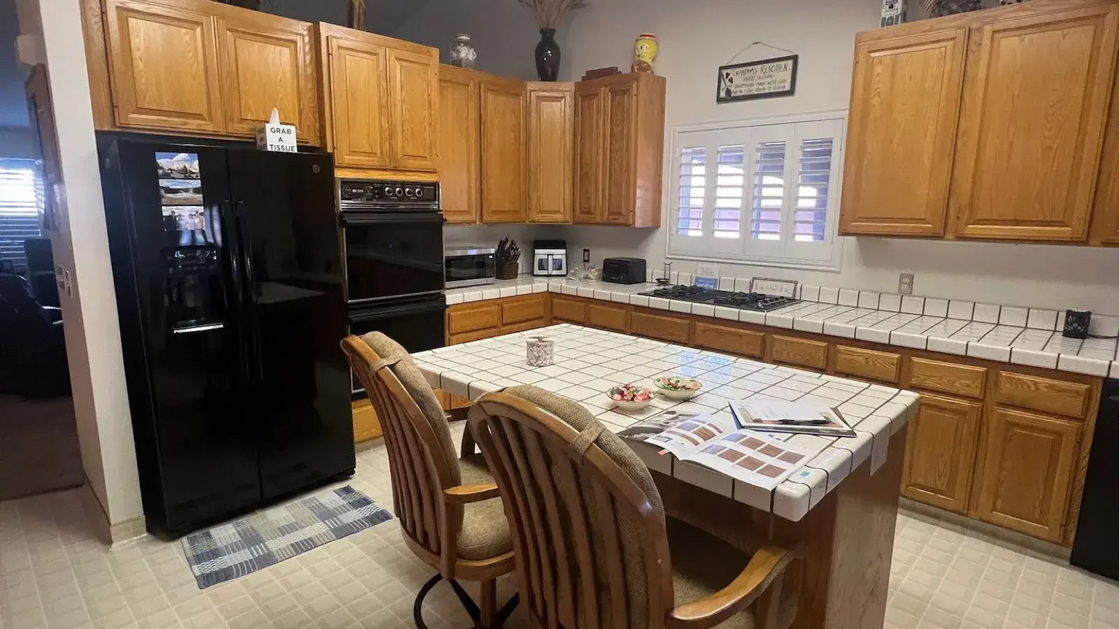 Before: Dated kitchen with oak cabinets, tile counters, and a fluorescent light box before remodel