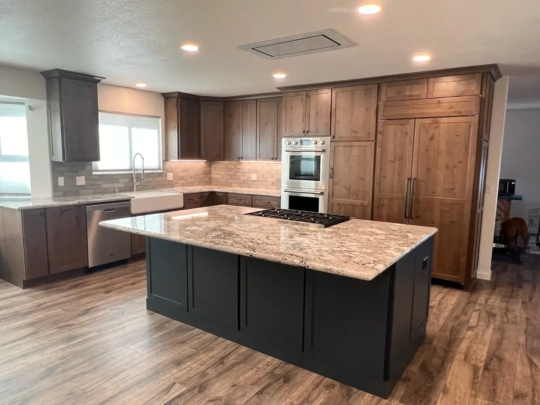 Kitchen island topped with polished granite, surrounded by knotty alder cabinetry
