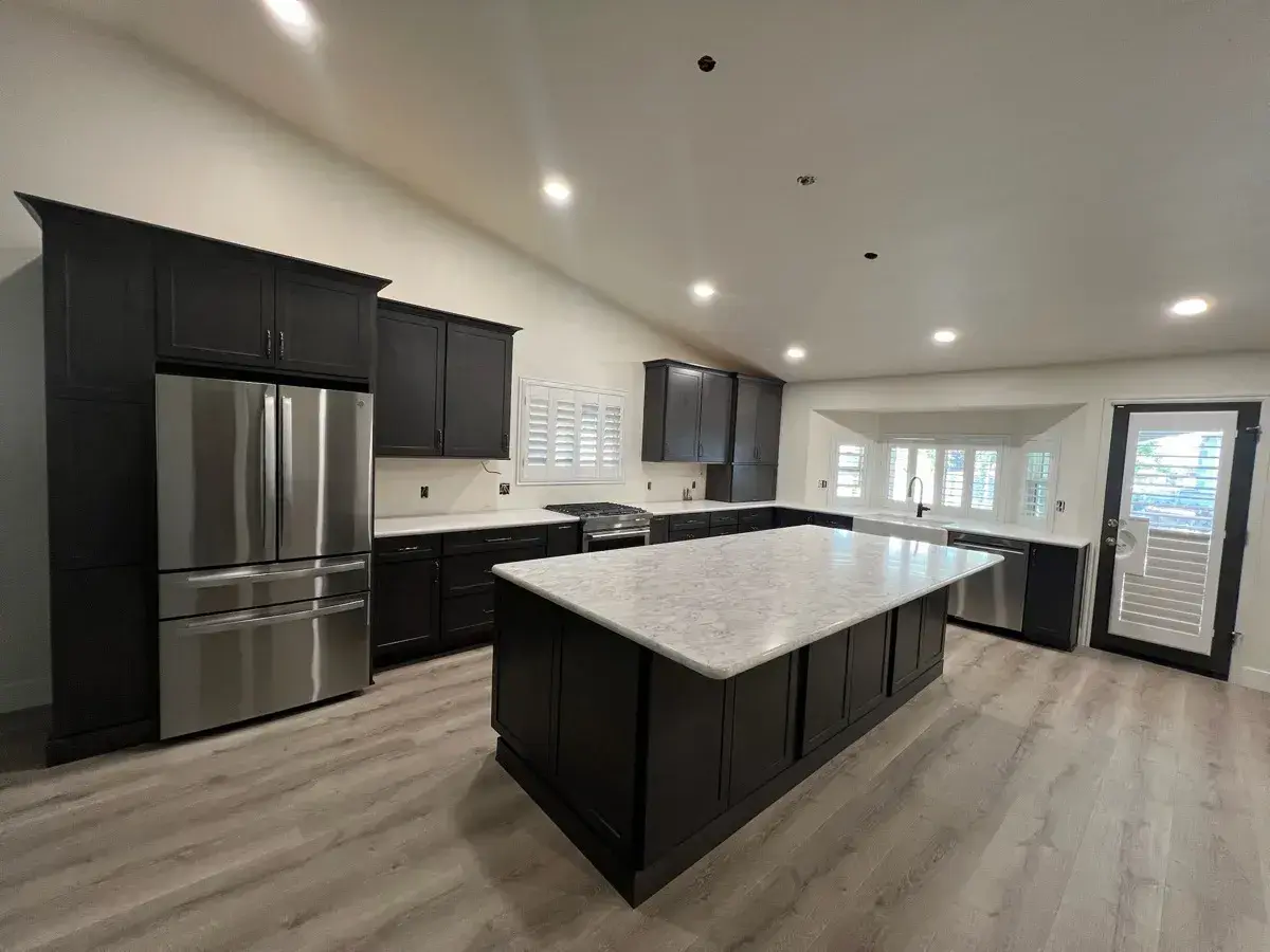 Remodeled open kitchen with charcoal cabinets, a marble island, and vaulted ceiling